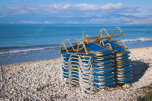 Stack of sunbeds chaise-longues piled up on the beach in the end of touristic season in Greece, Ionian sea islands
