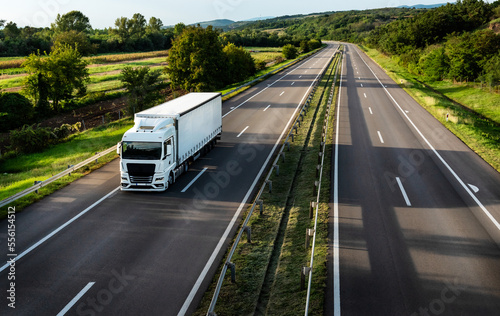 White truck driving on the highway winding through forested landscape in autumn colors at sunset