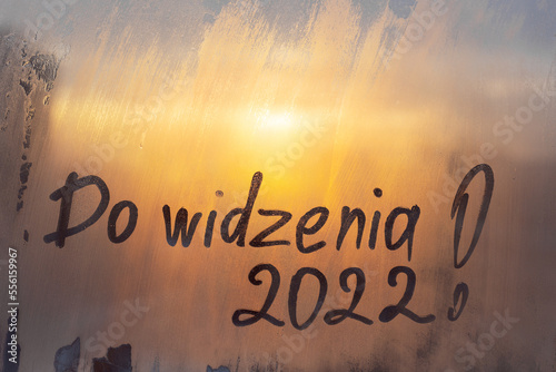 lettering Do widzenia in Polish is goodbye in english and numbers 2022 paint with finger of water on splashed by frost foggy glass on sunset window