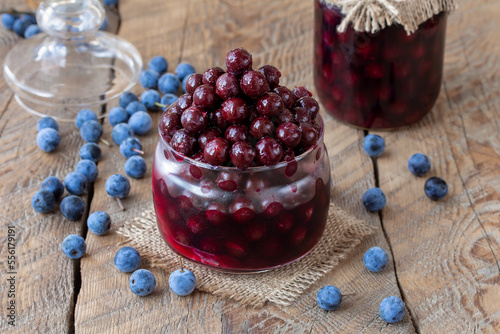 Homemade marinated Blackthorn or Sloe served in glass jar with fresh fruits on background. Selective focus, horizontal, wooden table.