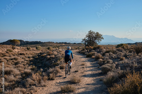 woman cyclist riding a gravel bicycle on the road in hills with mountain view, Alicante region in Spain 