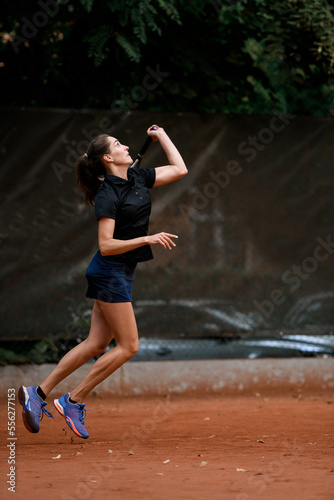 side view of an athletic female tennis player bouncing with racket and ready to hit tennis ball.