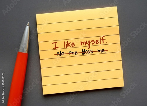 Yellow note paper on gray background with handwritten text NO ONE LIKES ME changed to I LIKE MYSELF - concept of develop growth mindset and turning negative self-talk into positive affirmation