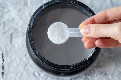 Close-up of a woman's hand with a measuring spoon of white BCAA powder. Protein shake for athletes and athletes