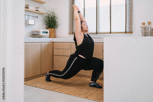fat woman raising hand forward lunge workout in kitchen. overweight determined woman in kitchen holding position move leg. fat motivated woman using weight down while raising hand up pose in kitchen