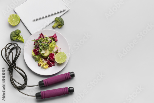 Plate with vegetable salad, skipping rope and notebook on grey background