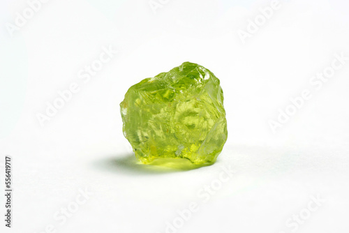 Natural chrysolite, peridot, olivine apple green color transparent raw rough crystal. Earth mined untreated, unheated, ready for faceting or cabochon making. Close-up on white paper background.