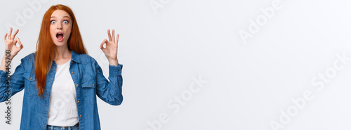 Amused, excited and thrilled good-looking redhead female in denim shirt, open mouth, drop jaw speechless staring with popped eyes camera, showing okay gesture in approval, white background