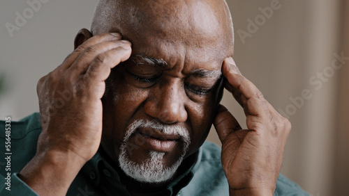 Close-up sad suffering elderly African American old sick ill man feeling headache chronic migraine bad pain unhealthy multiracial grandpa massaging temples middle-aged 60s retired male painful head