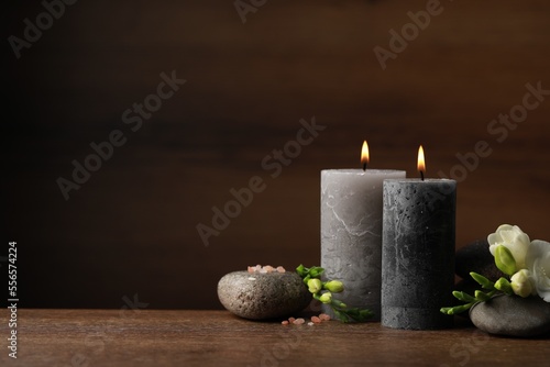 Beautiful composition with burning candles, spa stones and flowers on wooden table. Space for text