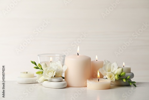 Beautiful composition with burning candles, spa stones and flowers on white table. Space for text