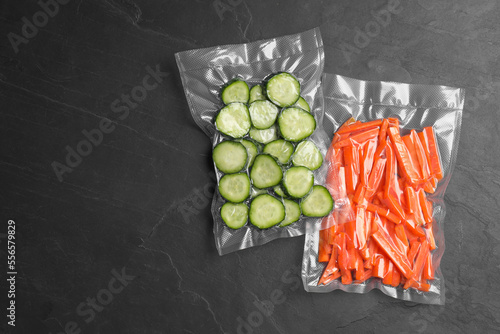 Sliced vegetables in vacuum packings on dark grey table, flat lay. Space for text