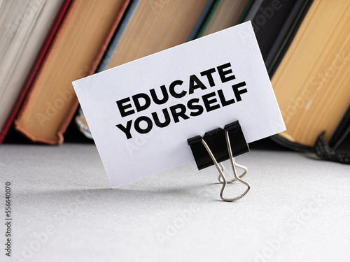 The message educate yourself written on a business card with books background. Self education training guidance or consultancy concept.