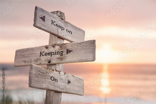 keep on keeping on text quote engraved on wooden signpost outdoors at the beach. Sunset theme.