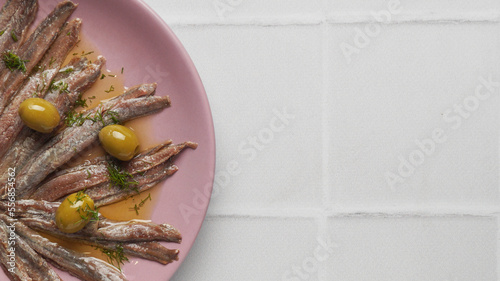 Canned anchovy fillets with olives on white tiled table, top view. Space for text
