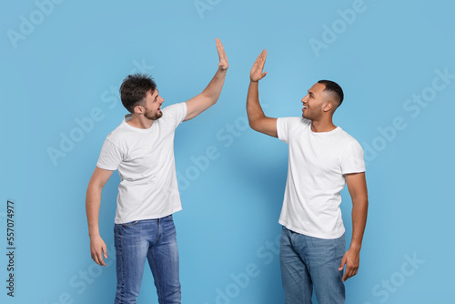 Men giving high five on light blue background