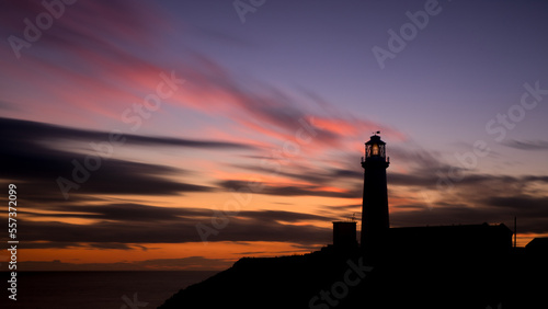 Lighthouse at sunrise with coloured sky and sea creating silhouette shape of lighthouse