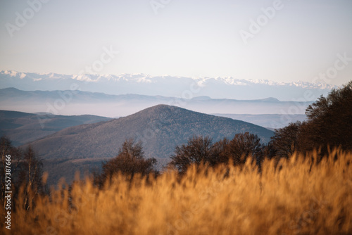 Sunrise landscape with dry grass meadow, high peaks and valley under vibrant colorful evening.
