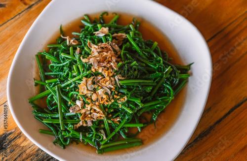 Stir-fried Phak Kut or Paco fern with garlic and oyster sauce. The healthy vegetable food menu of Thailand's traditional food, top view image food on white plate on wooden table.