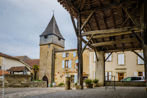 The main square, the wooden market hall and the church clock tower of the medieval village of Bassoues in the south of France (Gers)