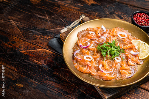 Italian Salmon carpaccio with onion and arugula served on a plate. Wooden background. Top view. Copy space