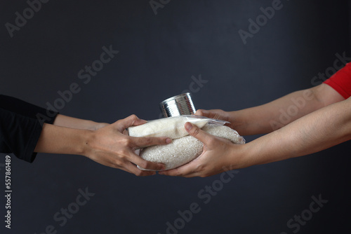 Hands giving and receiving staple food for donation and charity on dark gray background.