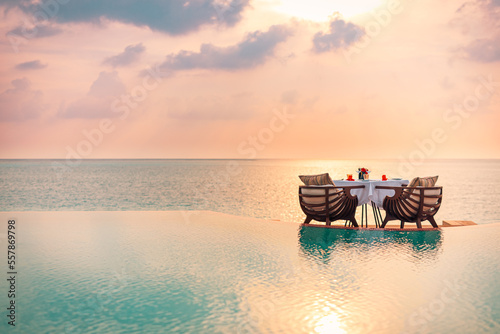 Seascape view under sunset light with dining table with infinity pool around. Romantic tranquil getaway for two, couple concept. Chairs, food and romance. Luxury destination dining, honeymoon template