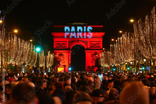 Paris, France - January 1st, 2023 : Crowd gathered on the Champs Elysées in Paris to celebrate the passing to 2023 with a fireworks show over the Arc de Triomphe (triumphal arch)