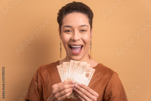 cheerful african american woman holding brazilian banknotes currency. in studio shot. business, income, loan, pay, wealth concept. 
