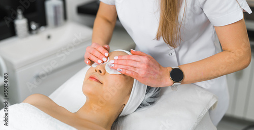 High-angle shot of a woman in a towel laying down while a beautician is putting an eye compress on her face. Beauty concept. High quality photo