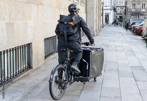 Courier man riding a cargo bike along the city on his way to deliver a package