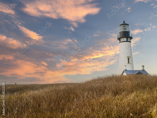 A lighthouse on a high bank under a sky with pink storm clouds. Hilly area with brown withered grass. Beautiful landscape. Tourism, travel, romance, history.