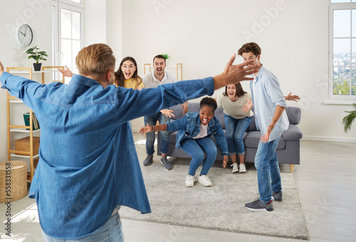 Happy friends reunite and have fun. Diverse group of excited young people meet friend who they haven't seen for very long time. Back view of happy man spreading his arms wide open to hug his friends