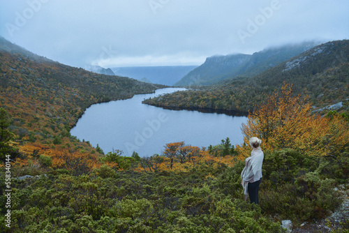 Woman standing with blanket scarf around her looking at lake from mountaintop view