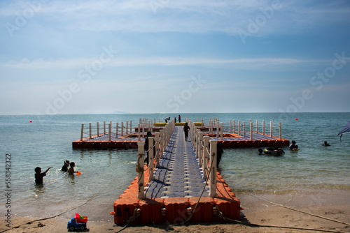 Thai people and foreign travelers travel visit play sand and swimming wave water in sea with plastic pontoons pier ocean of Bangsaen Beach at Chon Buri city on November 8, 2022 in Chonburi, Thailand