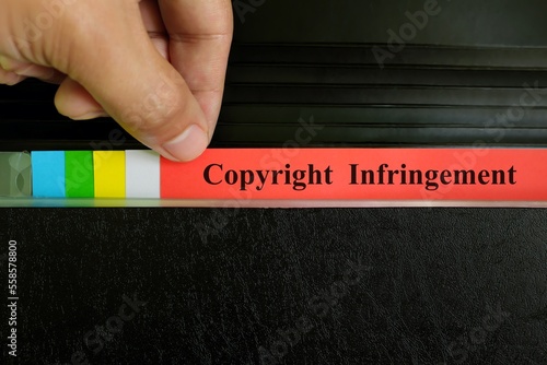 Hand picking copyright infringement file record in black binder folder. Copyright violation business legal concept. 