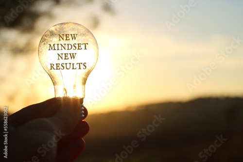 Hand holding light bulb with the text new mindset in front of the bright sun