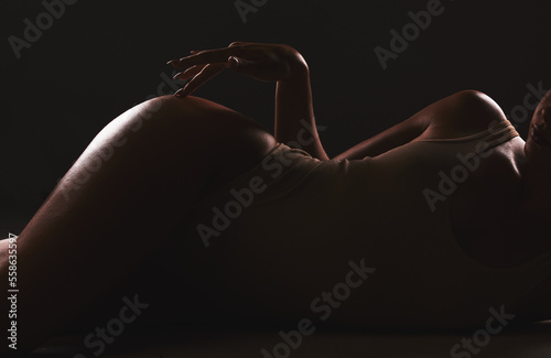 Lingerie, shadow and silhouette of sexy woman relax in erotic, sexual and seductive underwear on dark black background. Sexuality, creativity and body of aesthetic model girl with creative beauty