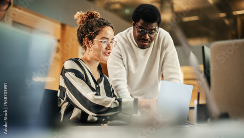 Portrait of Two Creative Colleagues Using Laptop to Discuss Work Project at Office. Young Black Technical Support Specialist Helping Female Customer Relationship Coordinator. Teamwork Concept