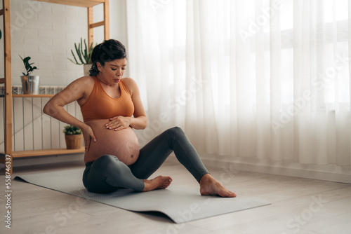 Young pregnant woman suffering from backache and having contractions while sitting on the floor at home.