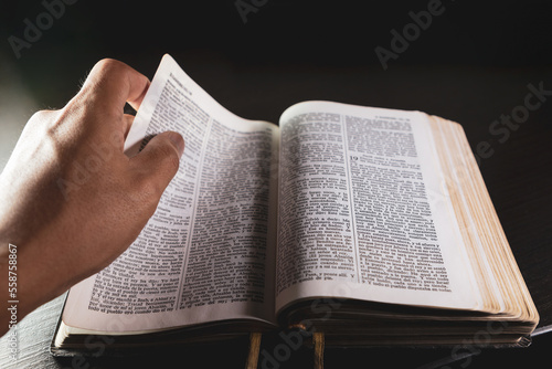 Leyendo la biblia, mano pasando de página, bendiciendo santa biblia y cruz de clavos en escritorio.