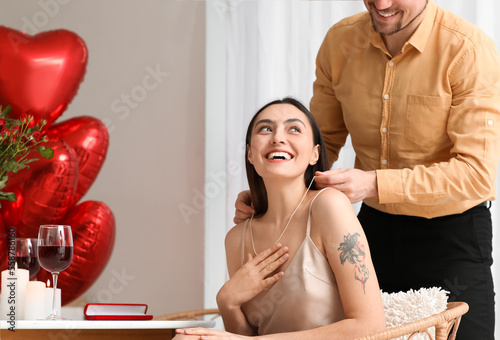Young man putting necklace around his girlfriend's neck in kitchen on Valentine's Day