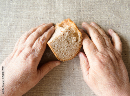 An old woman holds stale bread in her hands. Wrinkled hands of an old woman and a loaf of rye bread.A piece of dry bread on the table. The concept of social assistance to the poor. 