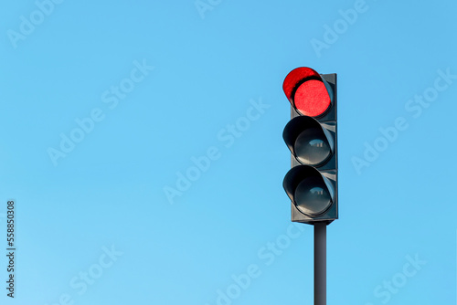 Modern traffic light with red light in front of cloudless sunny blue sky