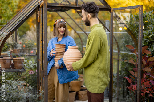 Man and woman take care of plants and flowers, gardening together in tiny orangery at backyard. Hobby or small family business of growing flowers concept