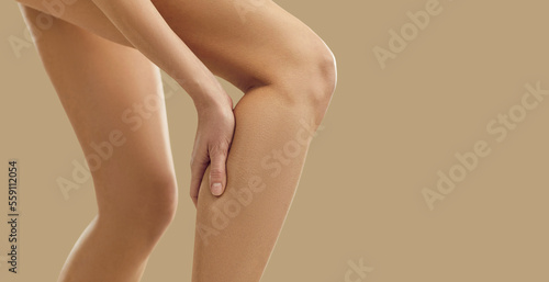 Woman feeling sudden pain in her leg. Young lady has a leg cramp and touches her calf. Female patient suffering from pain due to injured, torn, overstretched muscle. Injury concept. Copy space banner