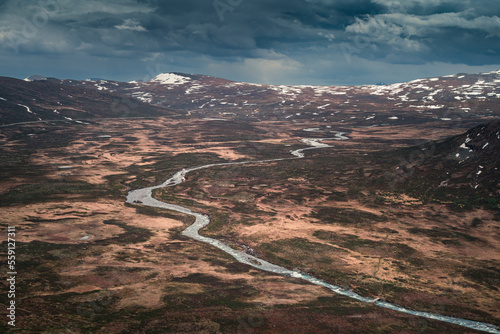 River Leirungsae with snow covered mountains in Jotunheimen National Park in Norway from above, dark clouds in sky