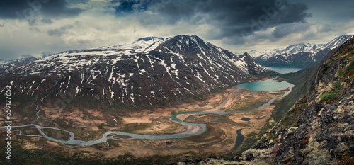 Turquoise lakes and river in mountain landscape from above the hike to Knutshoe summit in Jotunheimen National Park in Norway, snow-covered mountains of Besseggen in background