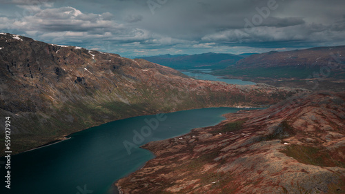 Blue lake in mountain landscape from above the hike to Knutshoe summit in Jotunheimen National Park in Norway, mountains of Besseggen in background, cloudy sky
