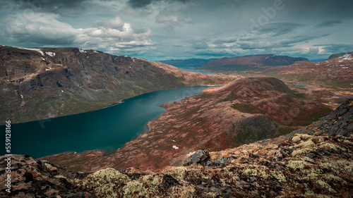 Blue lake in mountain landscape from above the hike to Knutshoe summit in Jotunheimen National Park in Norway, mountains of Besseggen in background, cloudy sky, moss in the foreground